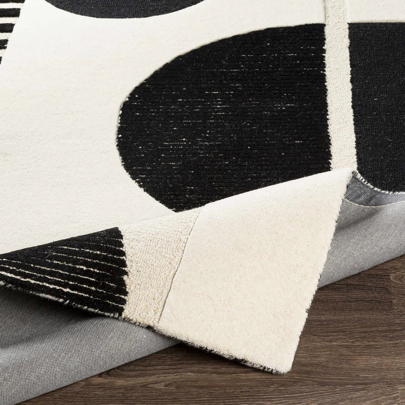 Close-up of black and ivory hand-tufted wool rug with geometric shapes and textured edge
