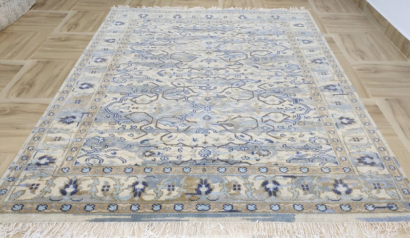 Transitional ikat floral wool rug on light wood floor, slate blue and cream with fringe